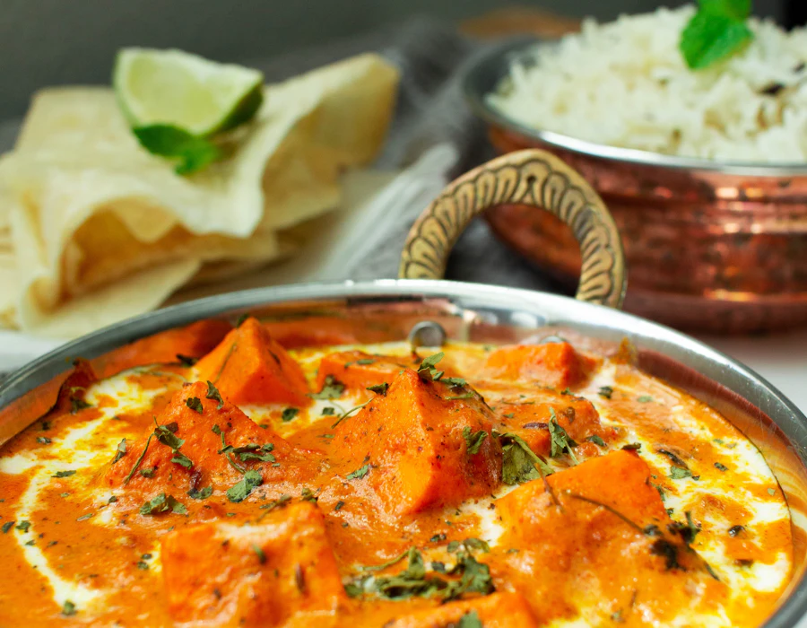 Creamy paneer makhani curry in a copper bowl with papad and rice